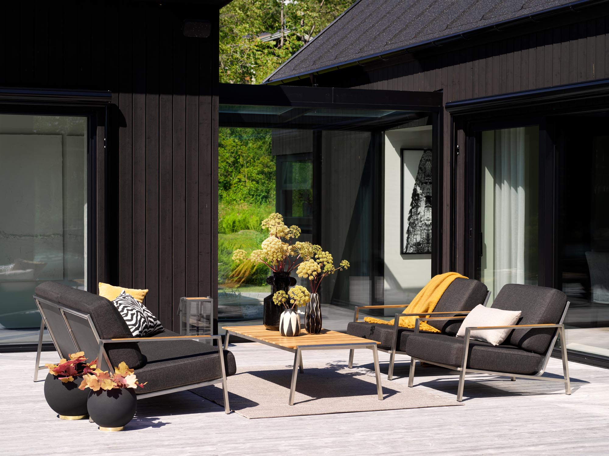 Modernes Lounge Sofa Naos mit edlem Edelstahlrahmen und warmen Teak-Armlehnen, perfekt für gemütliche Stunden im Garten.