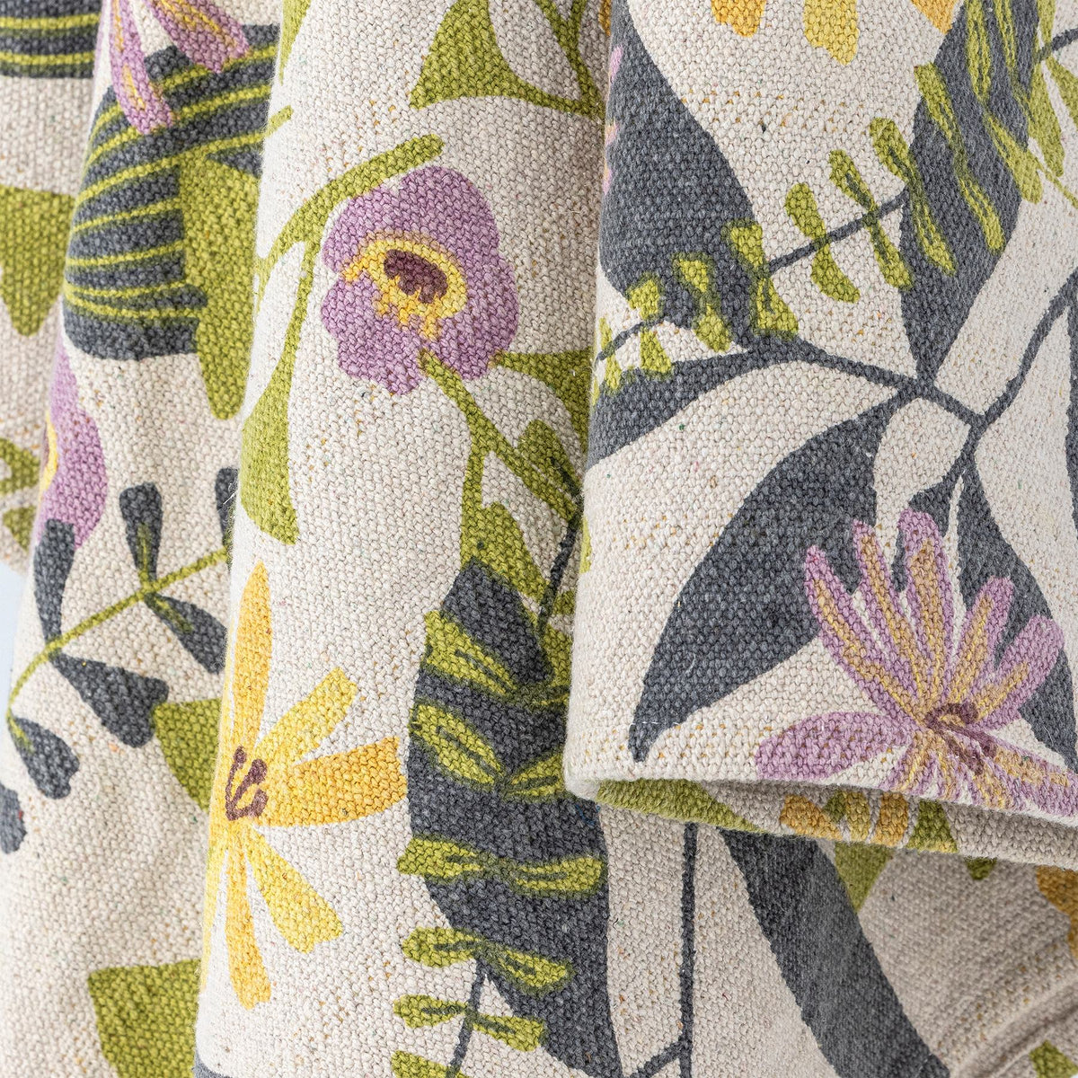 Wolldecke Camelie von Creative Collection in Bunt mit botanischem Blätter- und Blumenmuster, gewebt und bedruckt, mit gelben Quasten an den Ecken.