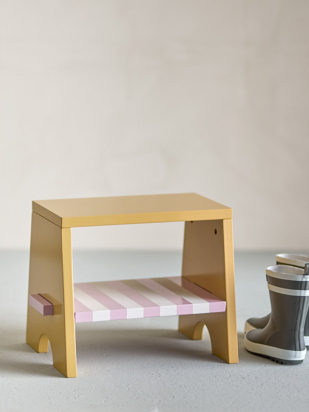 Liova Hocker von Bloomingville Mini aus lackiertem MDF, hellgelber Rahmen mit rosafarbenen Streifen auf der Sitzfläche, kleine Sitzgelegenheit.