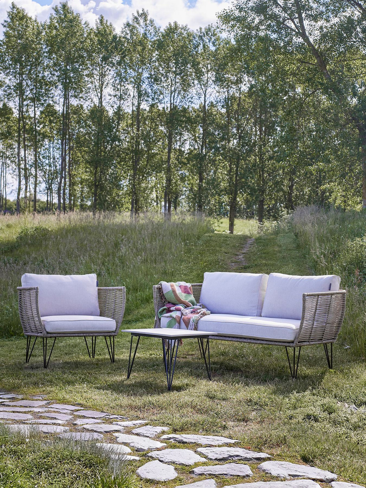 Braunes Lounge Sofa mit Flechtoptik, schwarzem Eisengestell und hellen Kissen, Modell Mundo von Bloomingville im Aussenbereich.