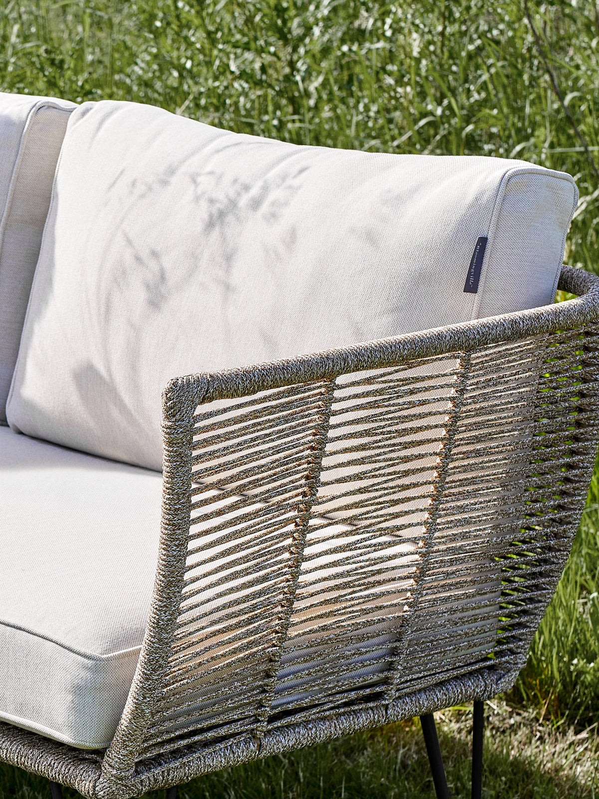 Braunes Lounge Sofa mit Flechtoptik, schwarzem Eisengestell und hellen Kissen, Modell Mundo von Bloomingville im Aussenbereich.