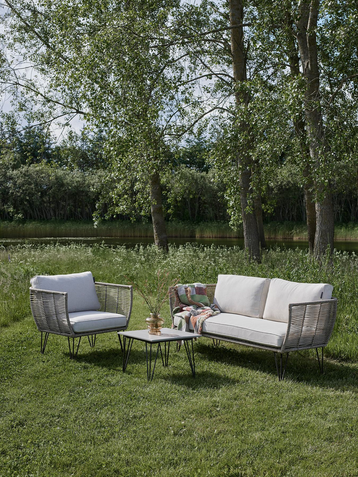 Braunes Lounge Sofa mit Flechtoptik, schwarzem Eisengestell und hellen Kissen, Modell Mundo von Bloomingville im Aussenbereich.