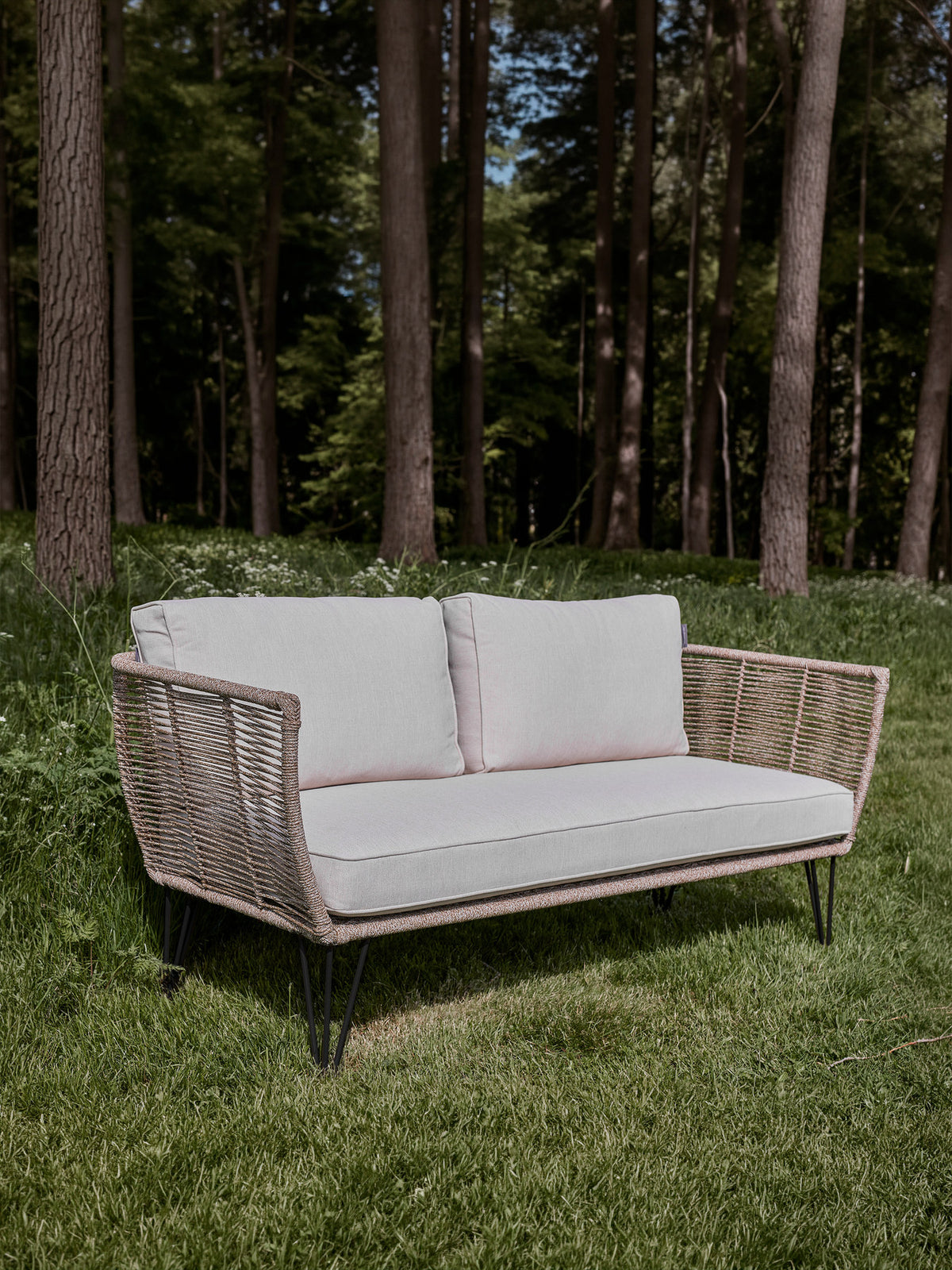 Braunes Lounge Sofa mit Flechtoptik, schwarzem Eisengestell und hellen Kissen, Modell Mundo von Bloomingville im Aussenbereich.