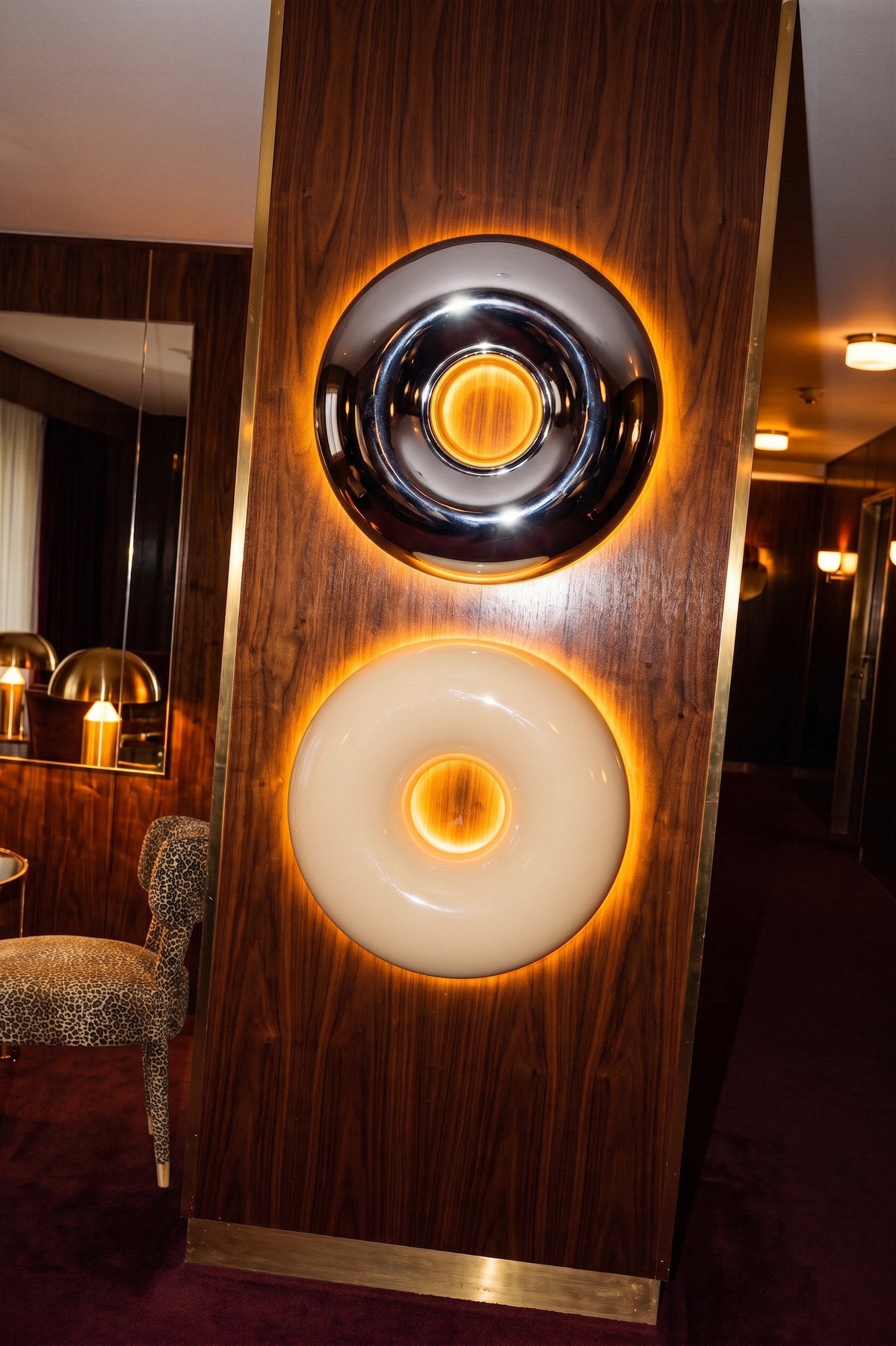 Runde beige Wandleuchte aus glänzendem Metall in Donut-Form mit indirektem Lichtaustritt entlang des Randes, montiert an einer Wand.