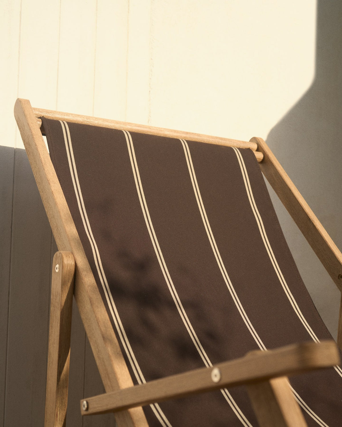 Braun-beige gestreifter Liegestuhl aus massivem Akazienholz mit klappbarem Gestell, Armlehnen und Stoffbespannung im Outdoor-Bereich.