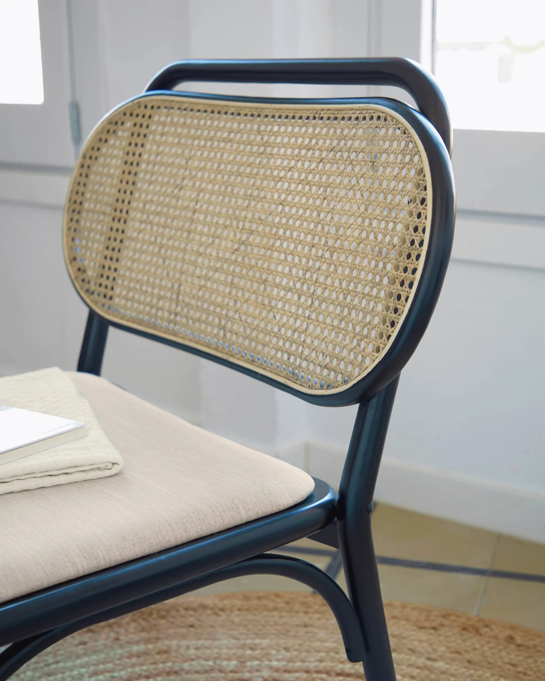Eleganter Sessel aus massiver Ulme mit schwarzem Finish, Rattanrücken und wasserabweisender Polsterung für stilvollen Komfort.