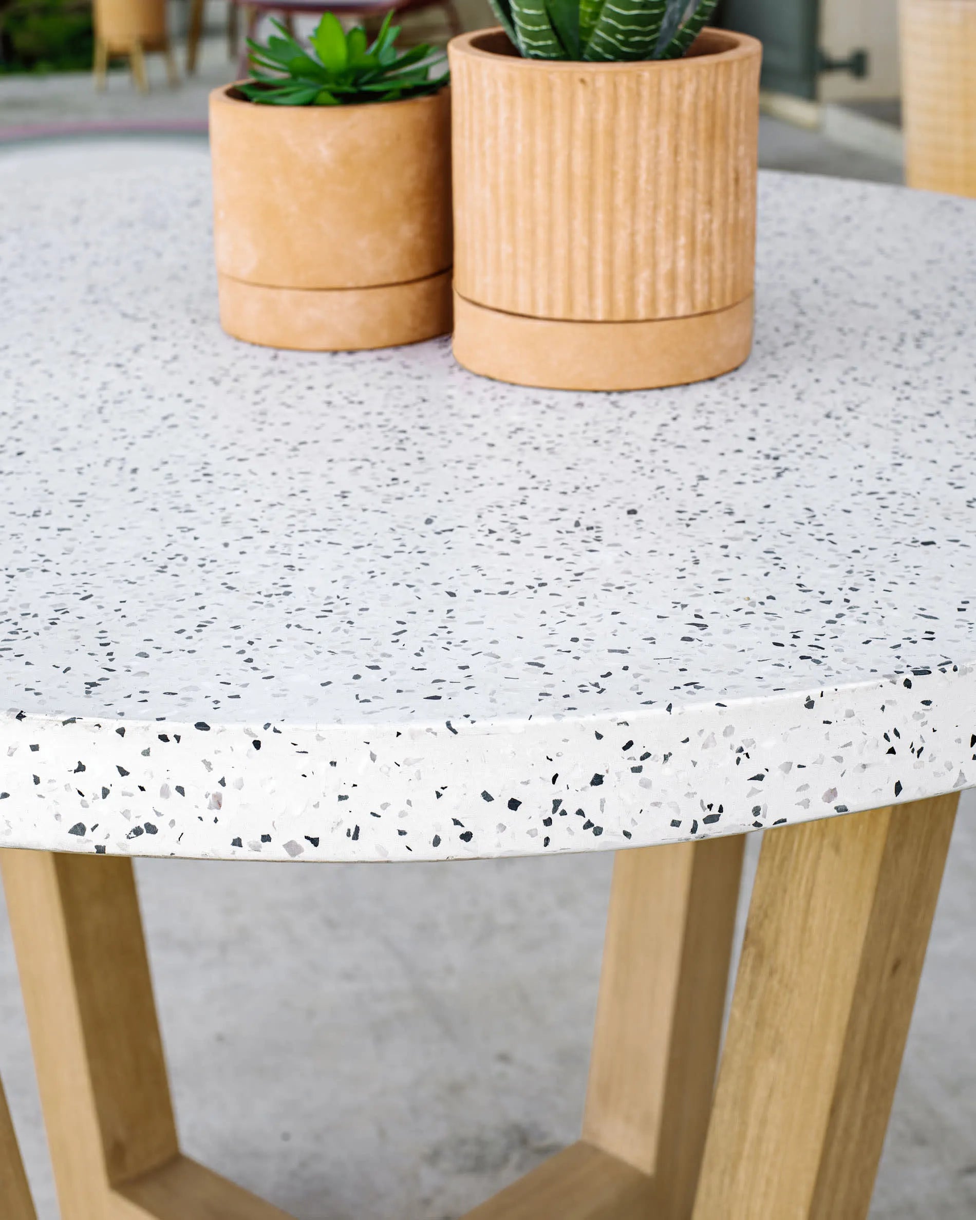 Eleganter runder Tisch aus weißem Terrazzo und Akazienholz, ideal für stilvolle Outdoor-Momente.