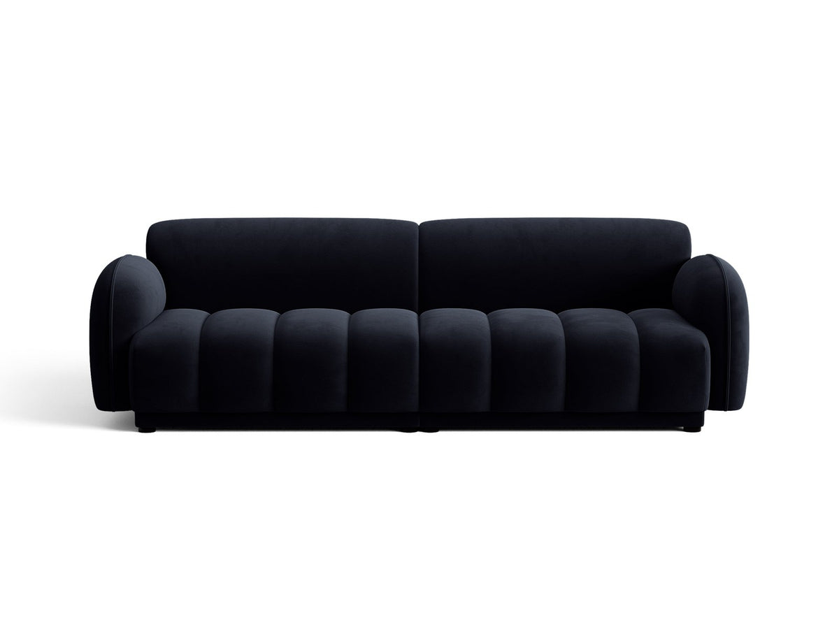 Vierersofa Bilbao mit hellbeigem Samtbezug, schwarzen Kunststoffbeinen und klarer, gerader Linienführung, fotografiert freistehend im Raum.
