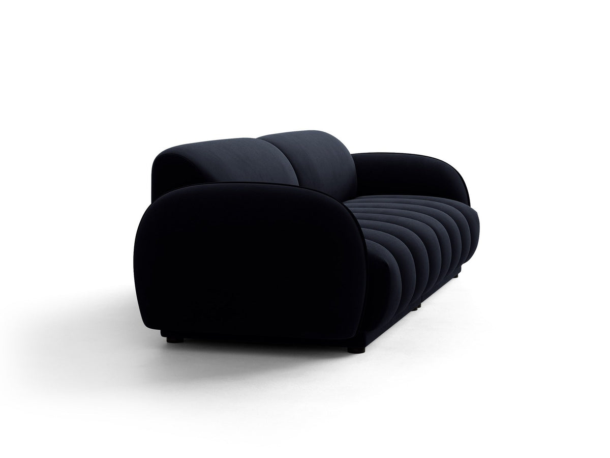 Vierersofa Bilbao mit hellbeigem Samtbezug, schwarzen Kunststoffbeinen und klarer, gerader Linienführung, fotografiert freistehend im Raum.