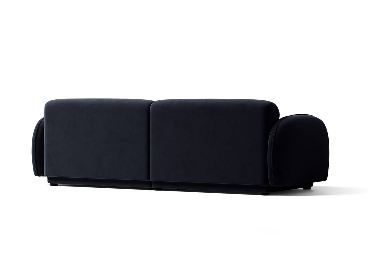 Vierersofa Bilbao mit hellbeigem Samtbezug, schwarzen Kunststoffbeinen und klarer, gerader Linienführung, fotografiert freistehend im Raum.