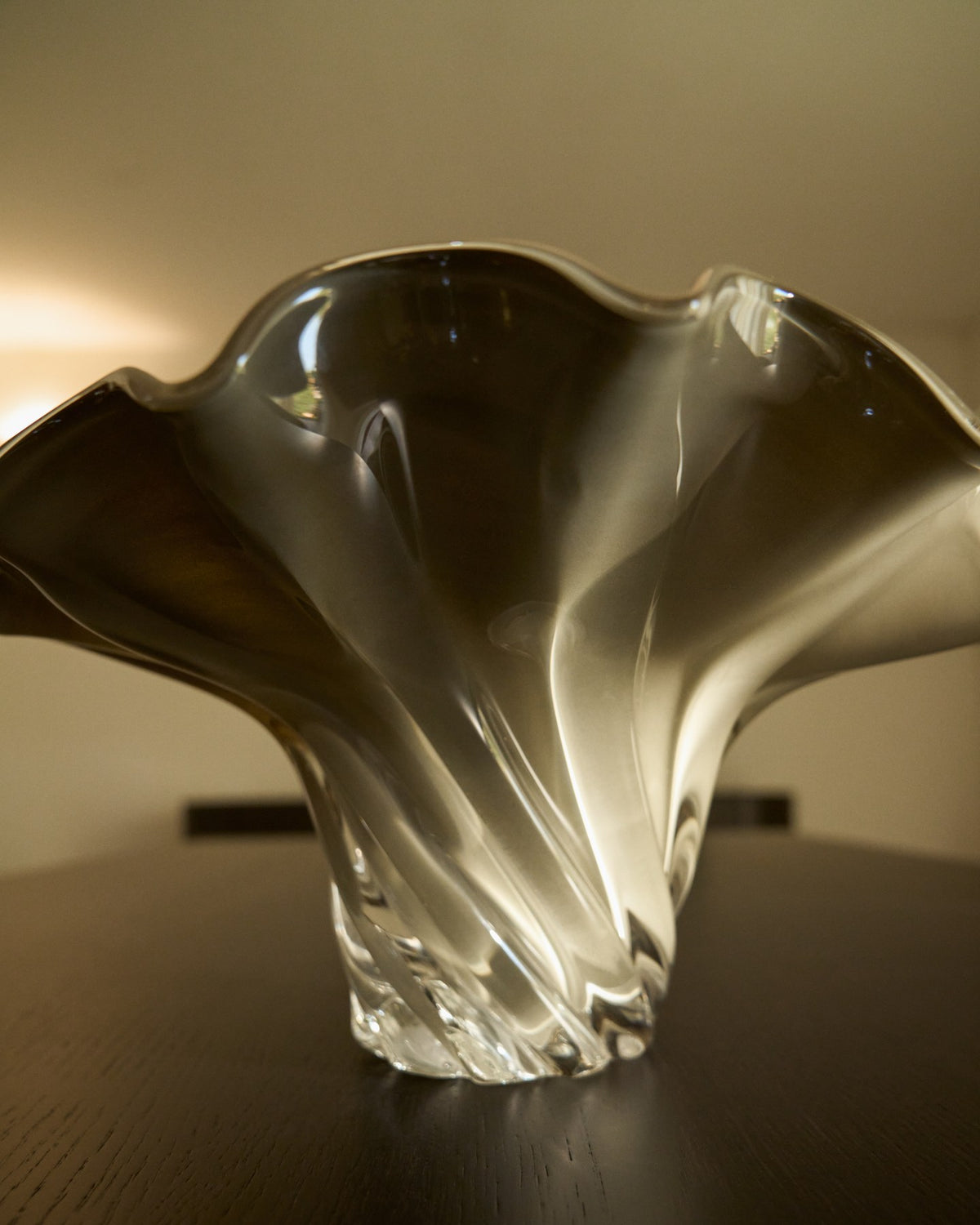 Foto eines handgefertigten Tafelaufsatzes aus hellgrünem, graugrün schimmerndem Glas mit geschwungener Wellenform und runder Öffnung.