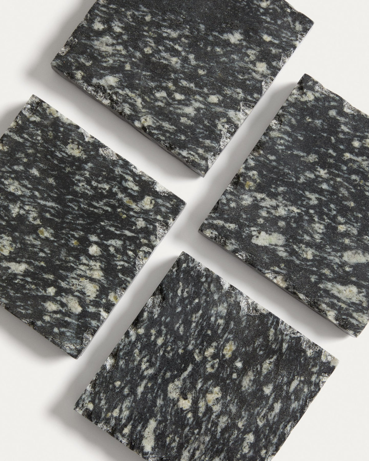 Vier quadratische Untersetzer aus dunkelgrauem Granit, handgefertigt mit natürlicher Marmorierung und individueller Textur, im Set von Kave Home.
