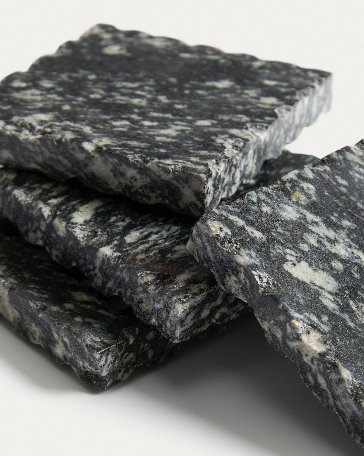 Vier quadratische Untersetzer aus dunkelgrauem Granit, handgefertigt mit natürlicher Marmorierung und individueller Textur, im Set von Kave Home.