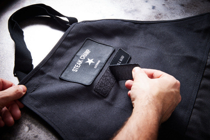 STEAK CHAMP Kochschürze 2 Taschen mit Klettverschluss für Beschriftung in Schwarz präsentiert im Onlineshop von KAQTU Design AG. Kochschürzen ist von STEAK CHAMP