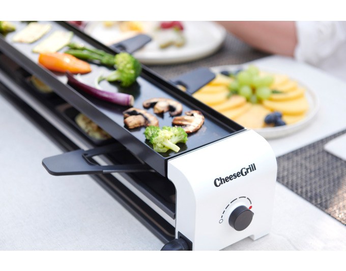Weisser Tischgrill STÖCKLI CheeseGrill 2 Connect mit wendbarer Aluguss-Grillplatte, zwei Pfännchen und Kunststoffspachtel auf hellem Untergrund.