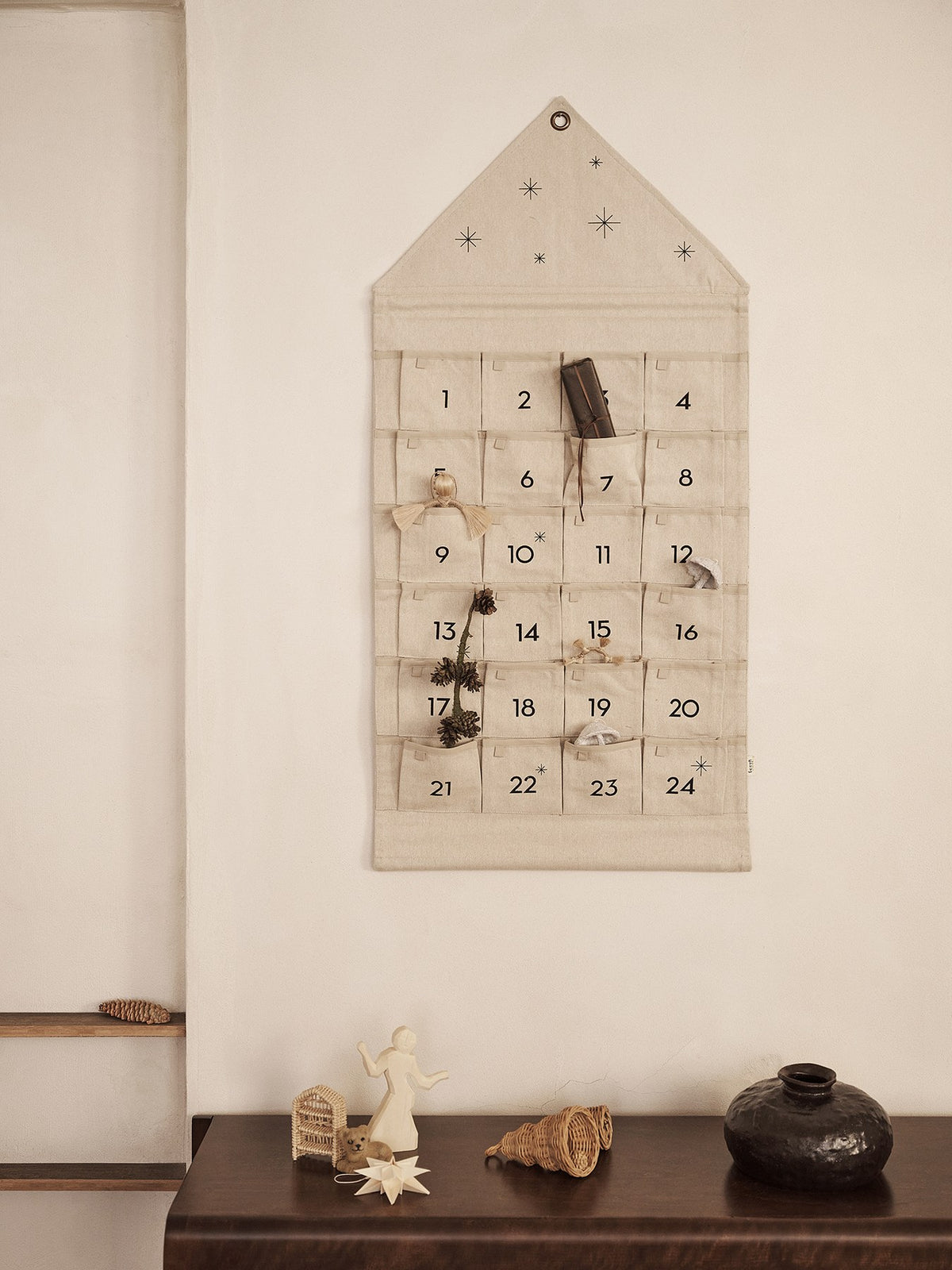 Textiler Adventskalender in Hausform aus gewebter Baumwoll-Chambray in Sand/Schwarz mit goldenen Stickereien und 24 kleinen Taschen für tägliche Geschenke.