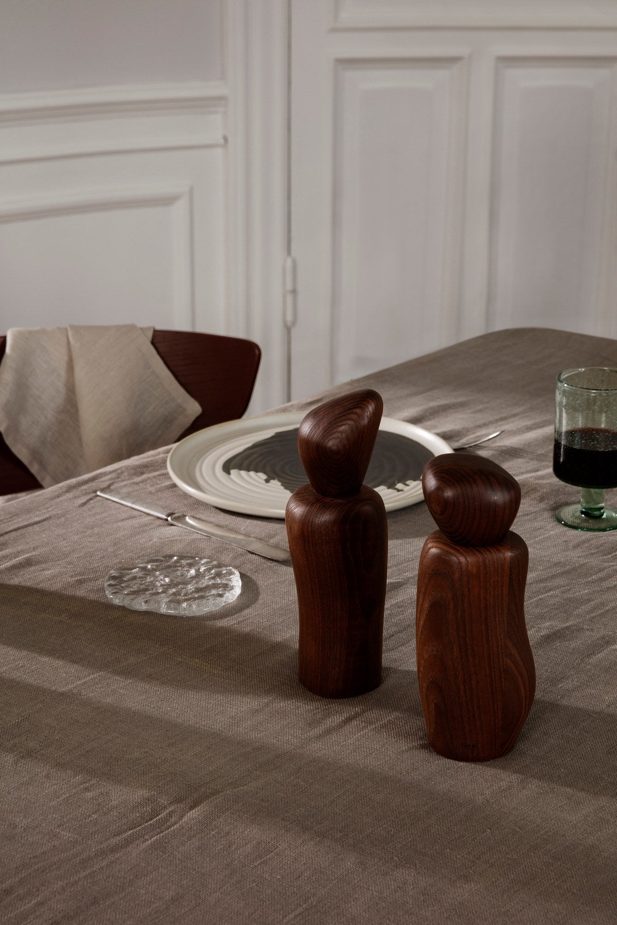 Kiesel-Mühle von Ferm Living in Dunkelbraun, FSC-zertifiziertes Eschenholz mit karbonisierter Oberfläche, kieselähnliche skulpturale Form auf hellem Hintergrund.