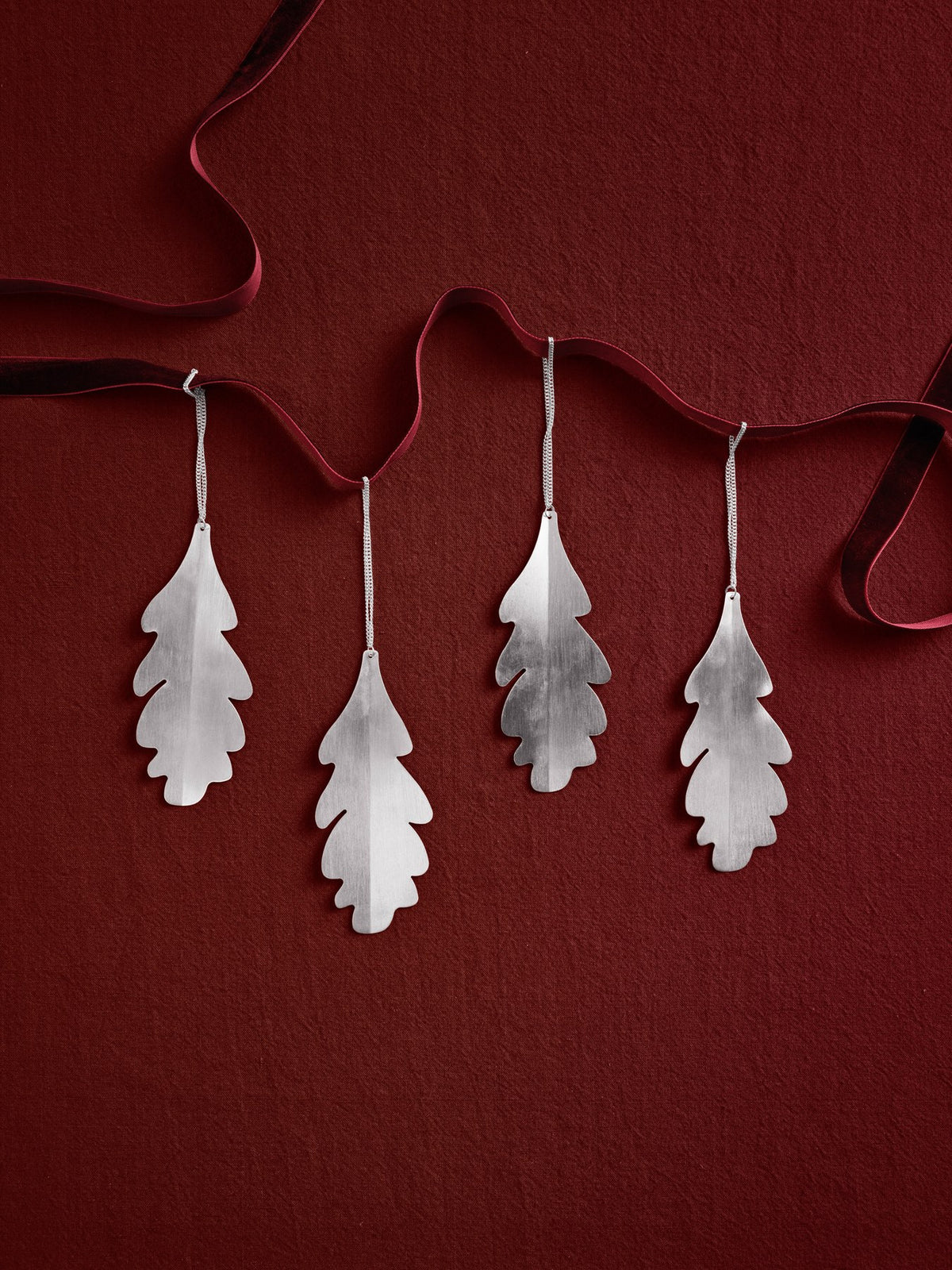 Vier silberne Eichenblatt-Ornamente aus versilbertem Massivmessing, blattförmig, glänzende Oberfläche, als Weihnachtsdekoration an Zweigen hängend.