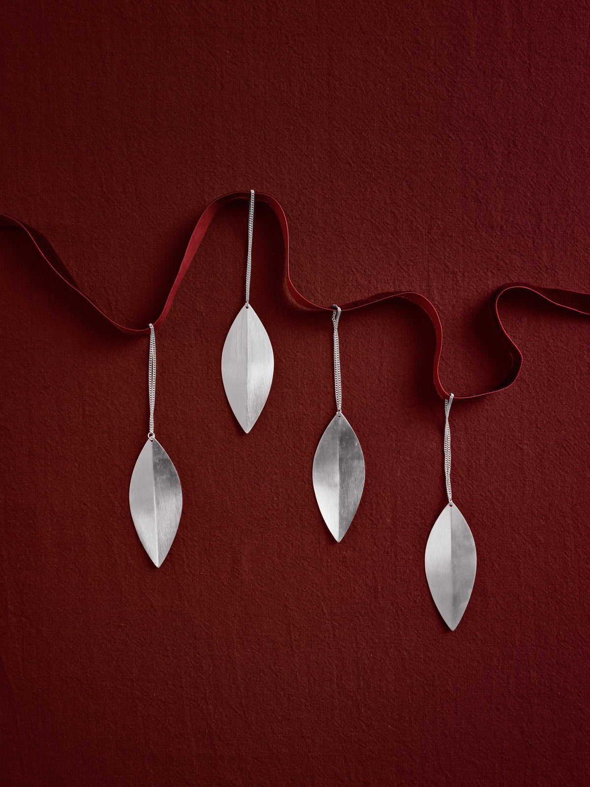 Vier blattförmige Weihnachtsornamente aus versilbertem Massivmessing von Ferm Living mit glänzender Oberfläche und schmuckartiger Form.