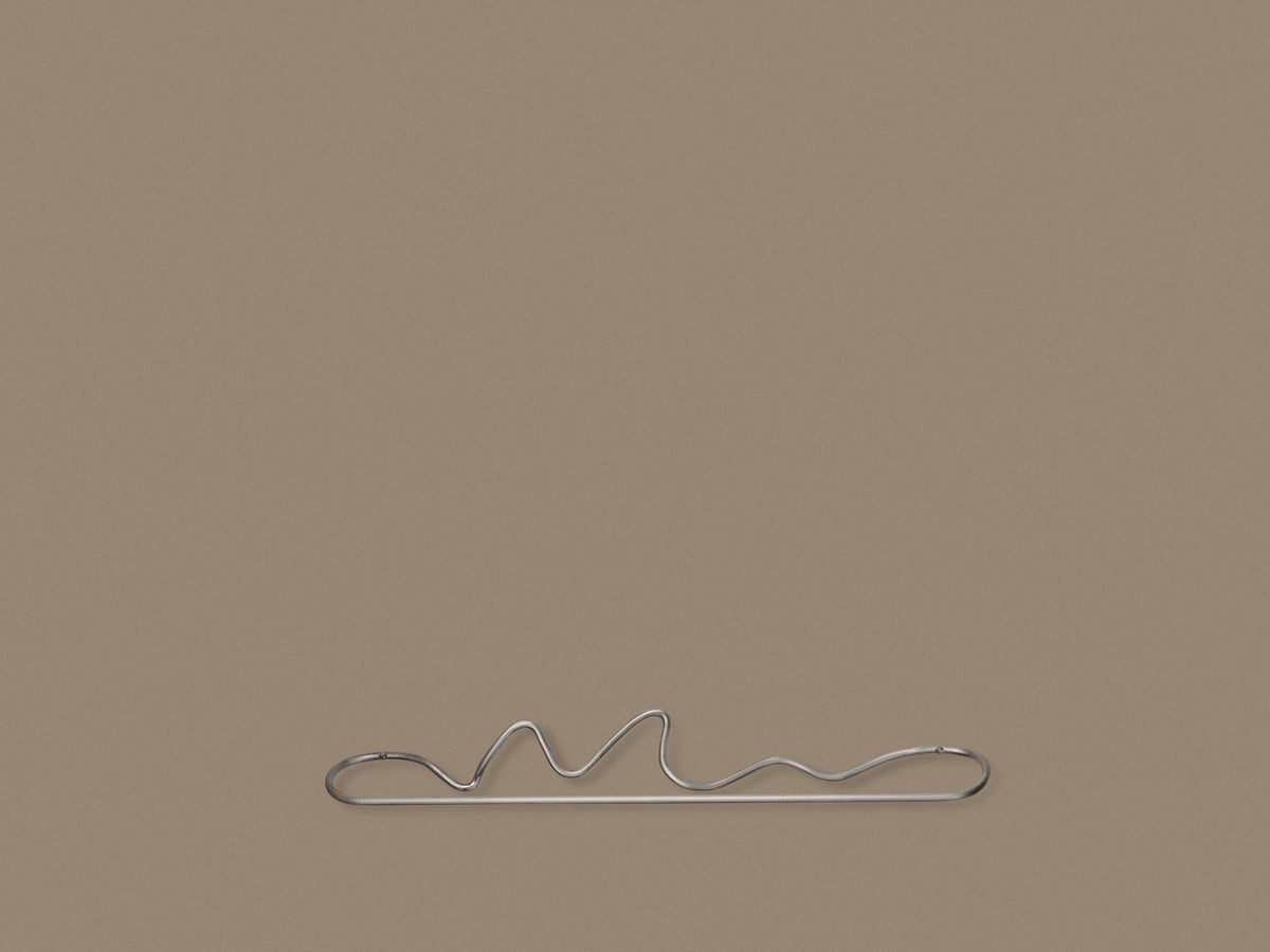 Curvature Handtuchhalter von Ferm Living aus Edelstahl mit geschwungener, skulpturaler Form, montiert an einer Badezimmerwand.