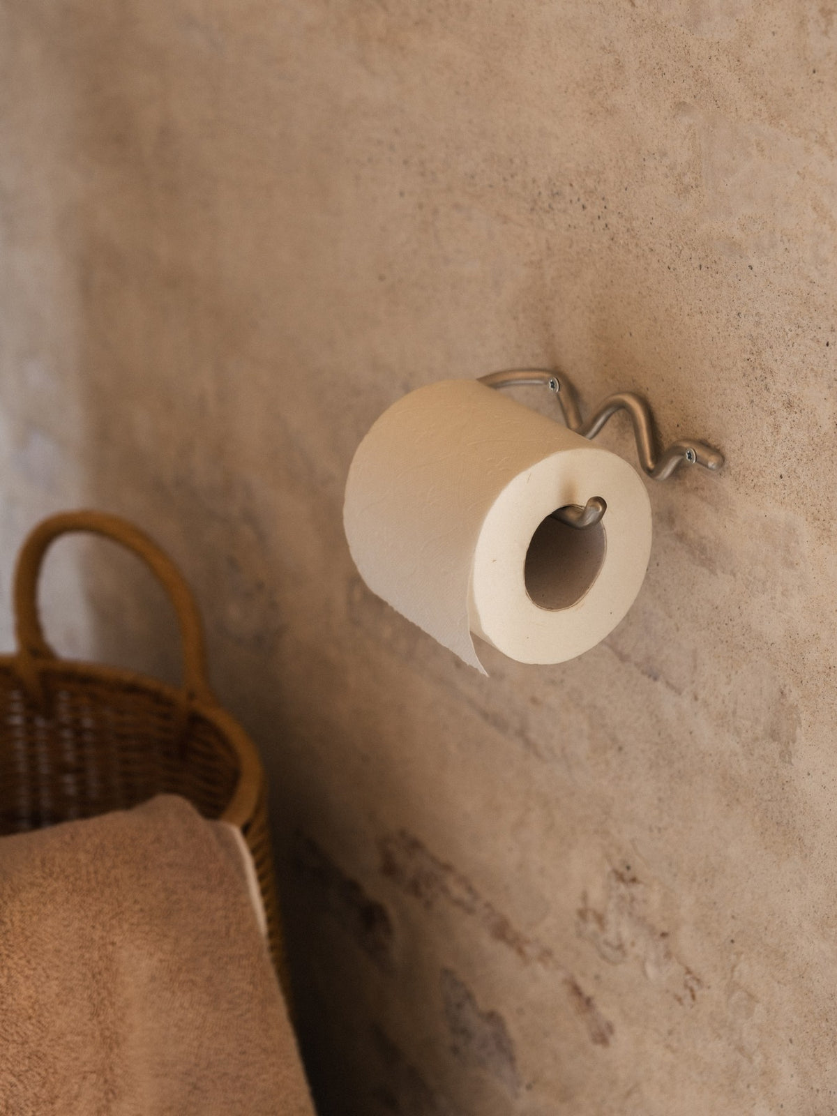 Wandmontierter Toilettenpapierhalter aus Edelstahl mit geschwungener, skulpturaler Form, handgefertigt von Ferm Living für das Badezimmer.