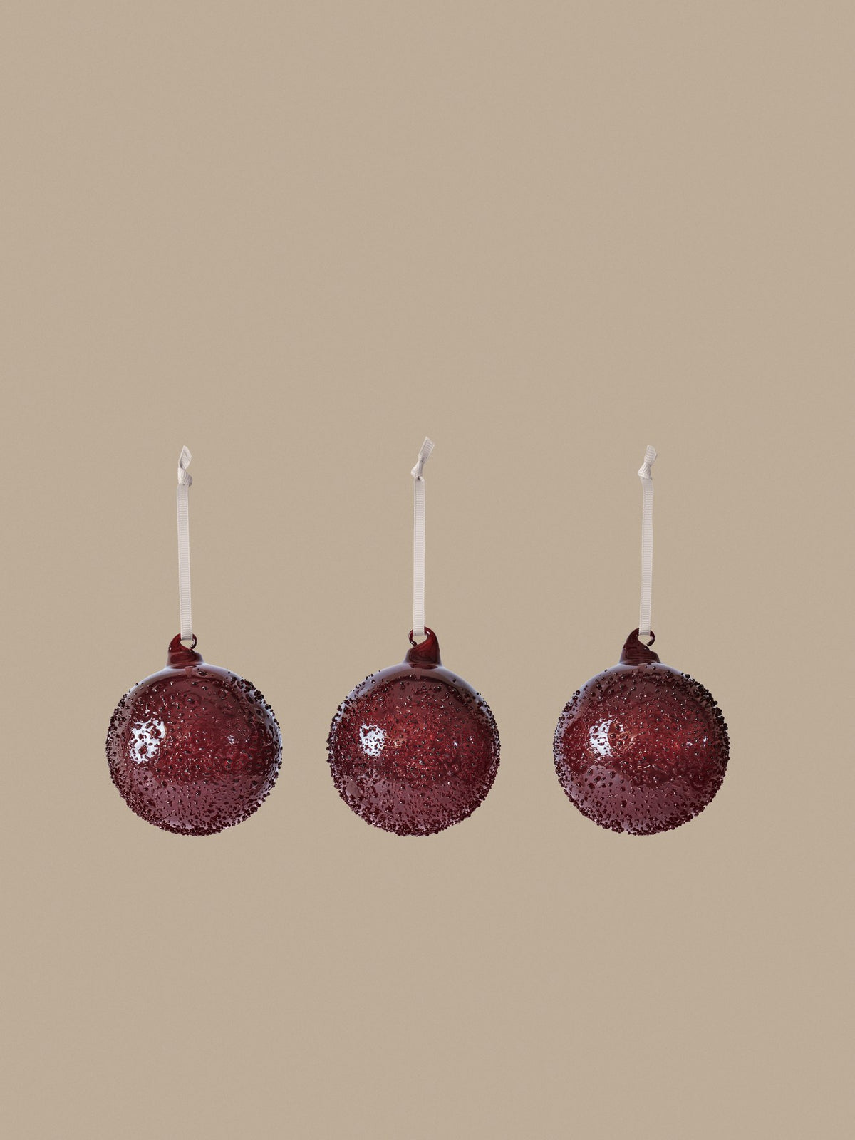Drei mundgeblasene Glaskugeln in Picante Rot mit strukturierter, kristalliner Oberfläche, Durchmesser 8 cm, an cremefarbenem Polyesterband hängend.