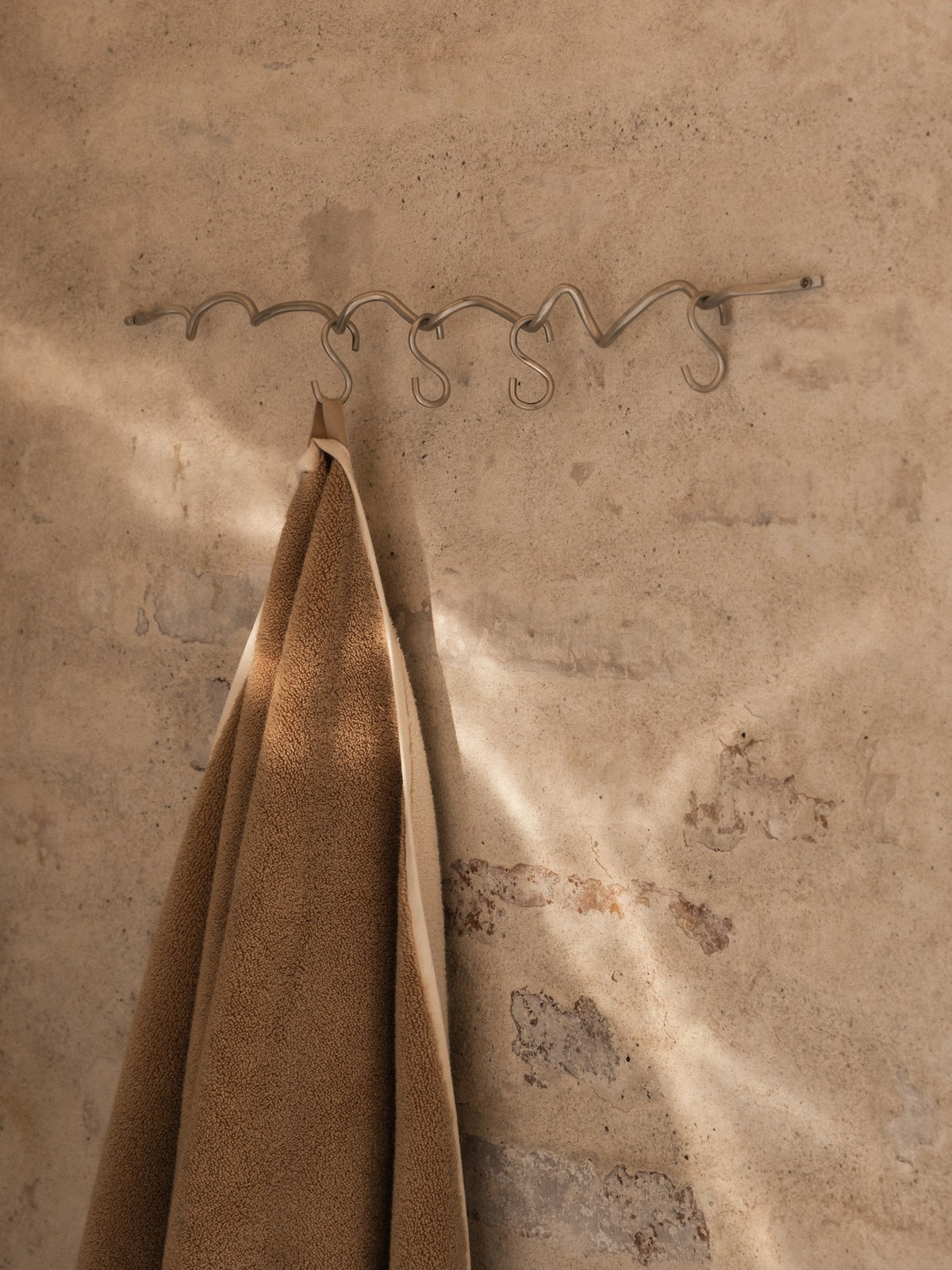 Produktfoto der Curvature Hängestange von Ferm Living aus massivem Messing mit matter Politur, inklusive sechs Haken, geschwungene Form.