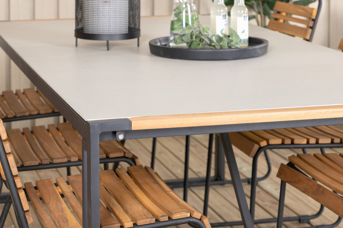 Rechteckiger Gartentisch mit schwarzer Glasplatte und Teakholz-Elementen, dazu zwei Esszimmerstühle mit Teakholz-Optik und Stahlgestell im Freien.