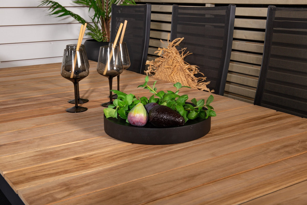 Zwei schwarze Relaxsessel Copacabana aus Aluminium mit Pulverbeschichtung neben rechteckigem Teak-Esstisch Mexico in Natur, Gartenmöbel-Set.