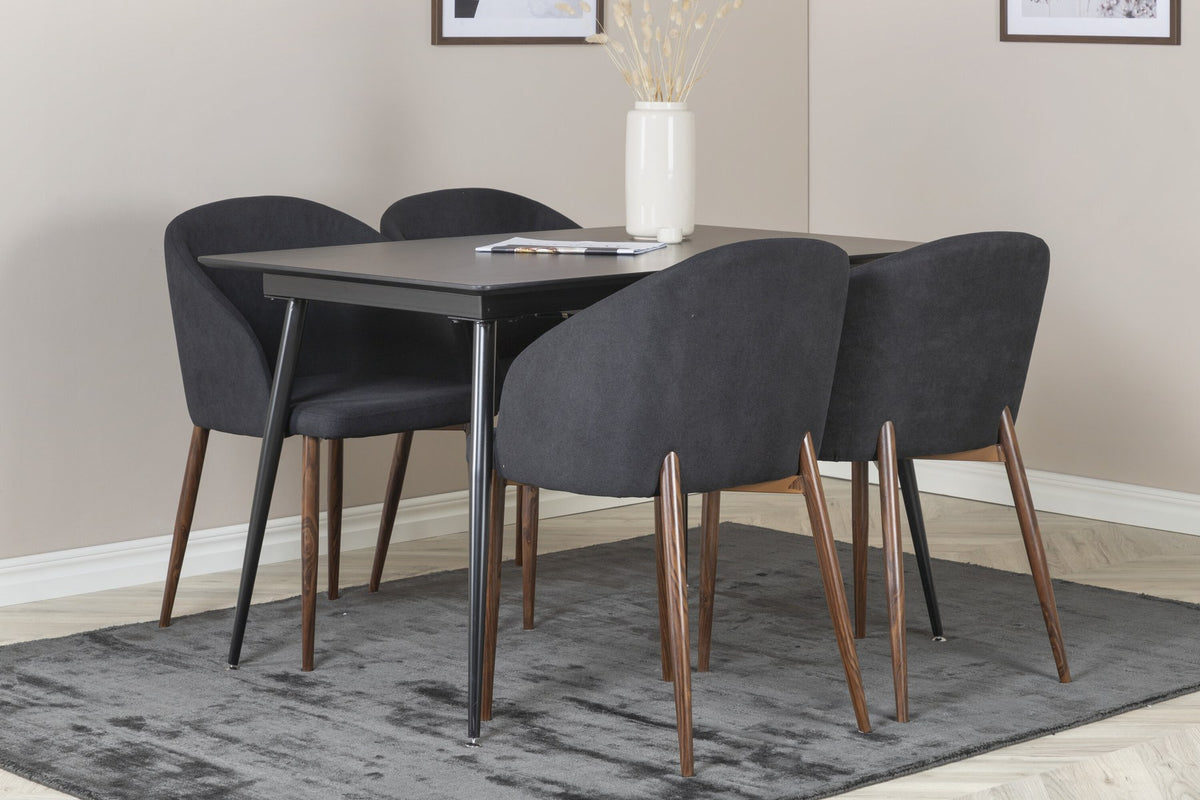 Rechteckiger Esstisch aus MDF und Stahl in Schwarz mit ausziehbarer Platte, daneben zwei Stühle mit Walnussbeinen und schwarzem Stoffbezug.