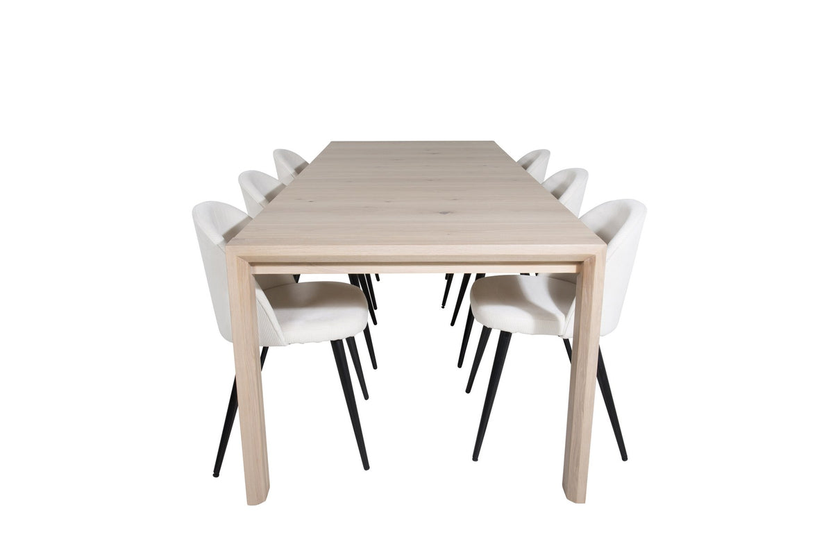 Esstisch mit heller Holzplatte in Naturfarbton auf Eichen-Gestell, umgeben von cremefarbenen Polsterstühlen aus Samt der Velvet-Serie.