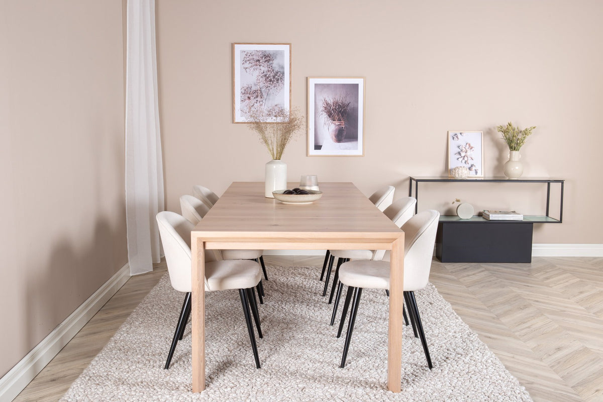 Esstisch mit heller Holzplatte in Naturfarbton auf Eichen-Gestell, umgeben von cremefarbenen Polsterstühlen aus Samt der Velvet-Serie.