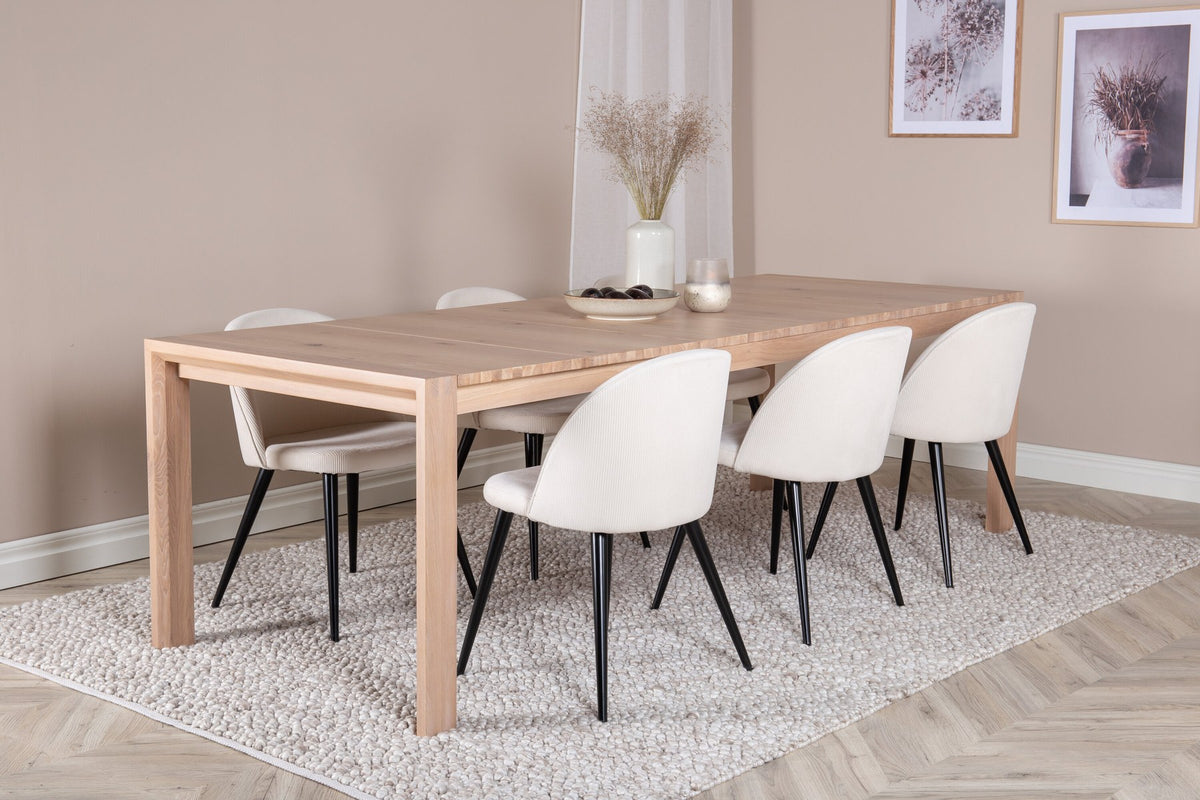 Esstisch mit heller Holzplatte in Naturfarbton auf Eichen-Gestell, umgeben von cremefarbenen Polsterstühlen aus Samt der Velvet-Serie.