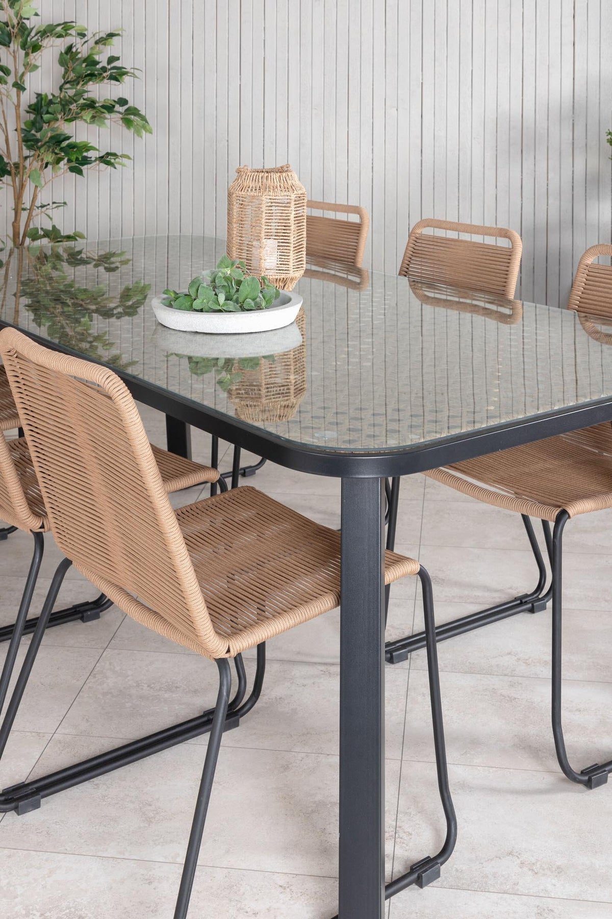 Gartentischset Paola mit schwarzem Stahlgestell und Weidengeflecht-Tischplatte sowie sechs stapelbaren Lindos-Stühlen aus schwarzem Aluminium und Polyesterseil.