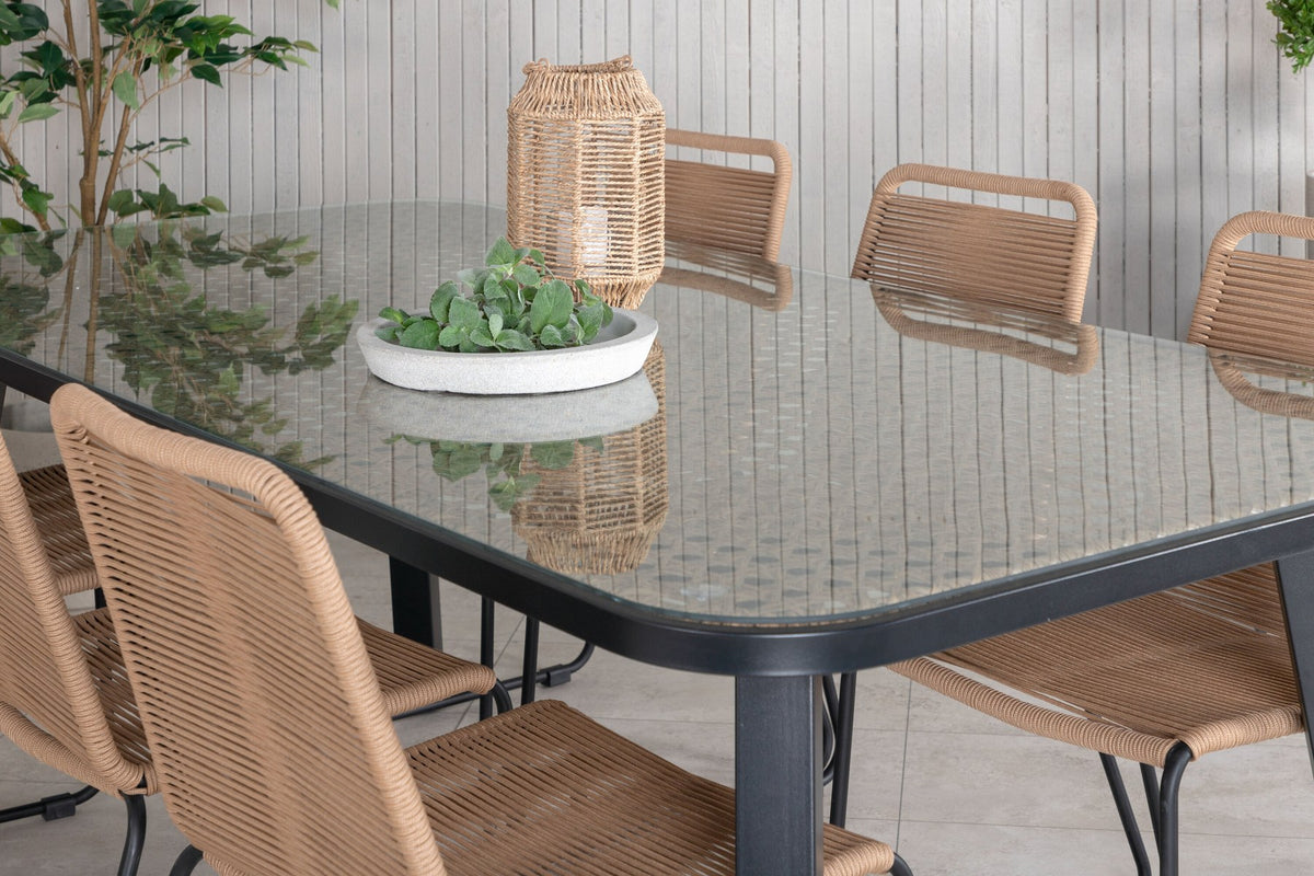 Gartentischset Paola mit schwarzem Stahlgestell und Weidengeflecht-Tischplatte sowie sechs stapelbaren Lindos-Stühlen aus schwarzem Aluminium und Polyesterseil.
