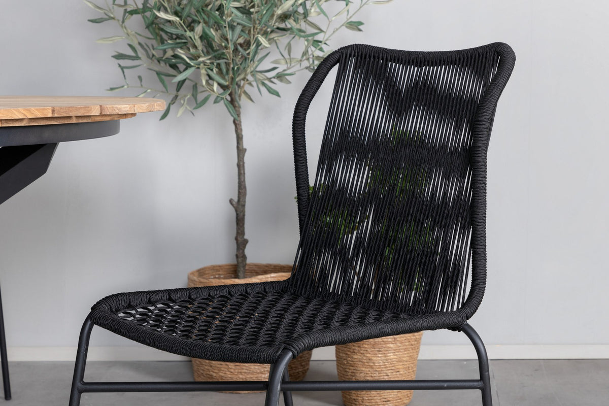 Vier schwarze Esszimmerstühle mit Aluminiumgestell und Polyesterbezug neben rundem Teak-Esstisch mit Stahlbeinen, Durchmesser 140 cm.
