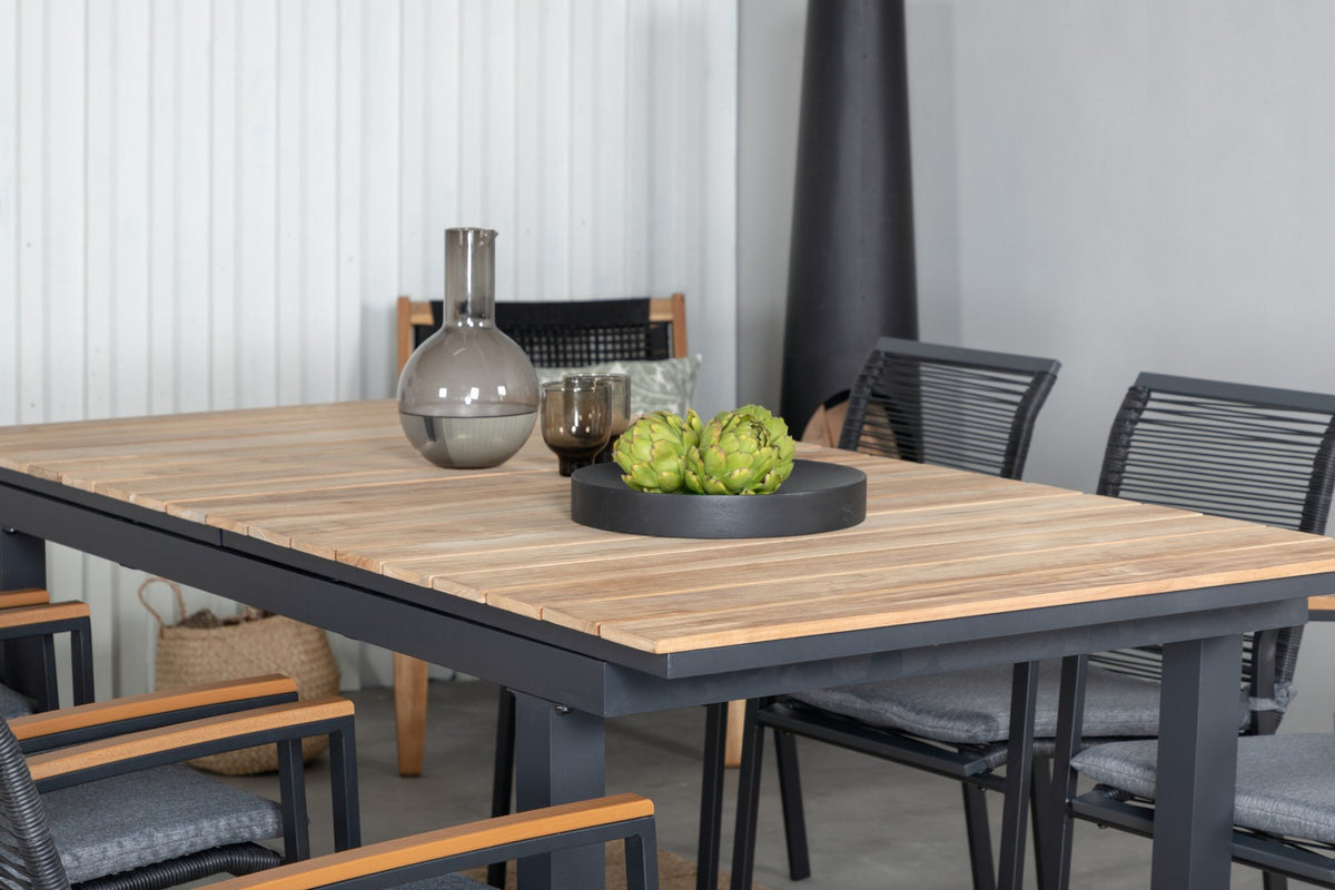 Foto eines schwarzen 2er-Stuhlsets mit Aluminiumgestell und Polyesterbezug neben einem rechteckigen Teak-Esstisch in Natur mit Stahlbeinen.