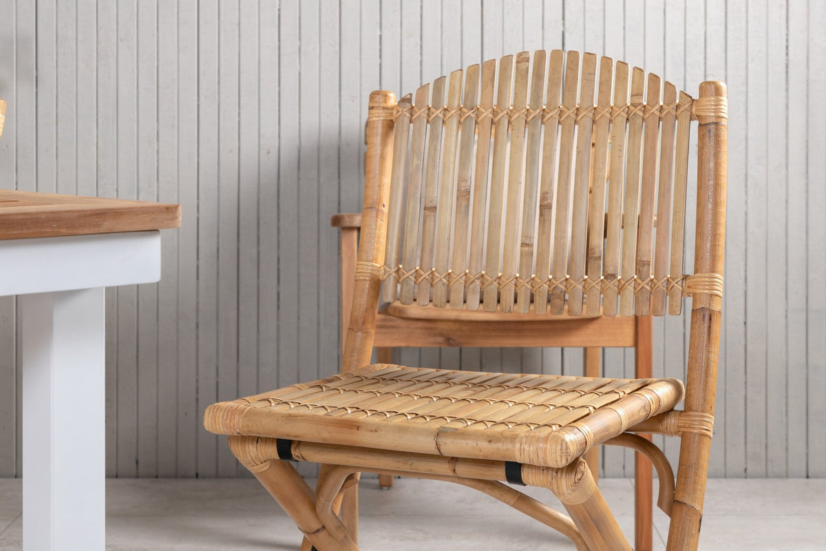 Foto zeigt einen Cafe Stuhl mit Rattan-Beinen und Stoffbezug in Natur sowie einen rechteckigen Teakholz-Esstisch mit weissem Aluminiumgestell.