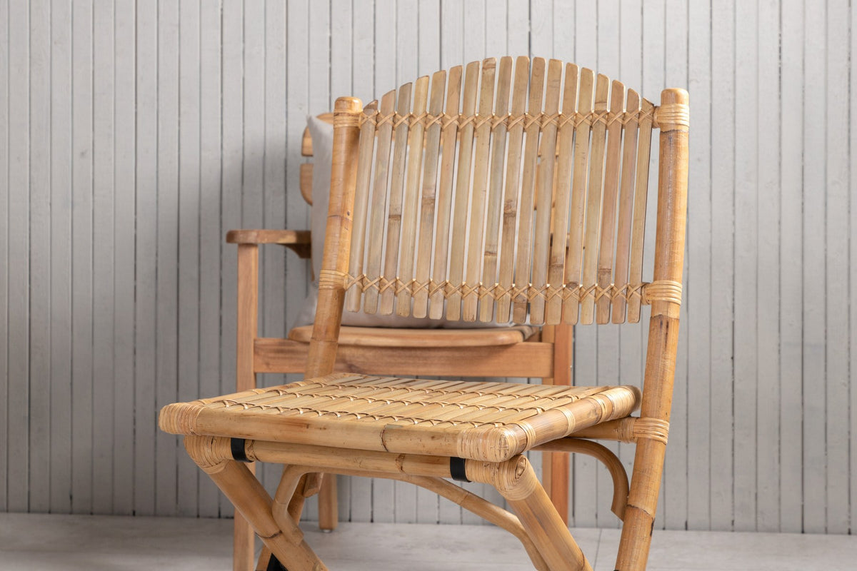 Foto zeigt einen Cafe Stuhl mit Rattan-Beinen und Stoffbezug in Natur sowie einen rechteckigen Teakholz-Esstisch mit weissem Aluminiumgestell.