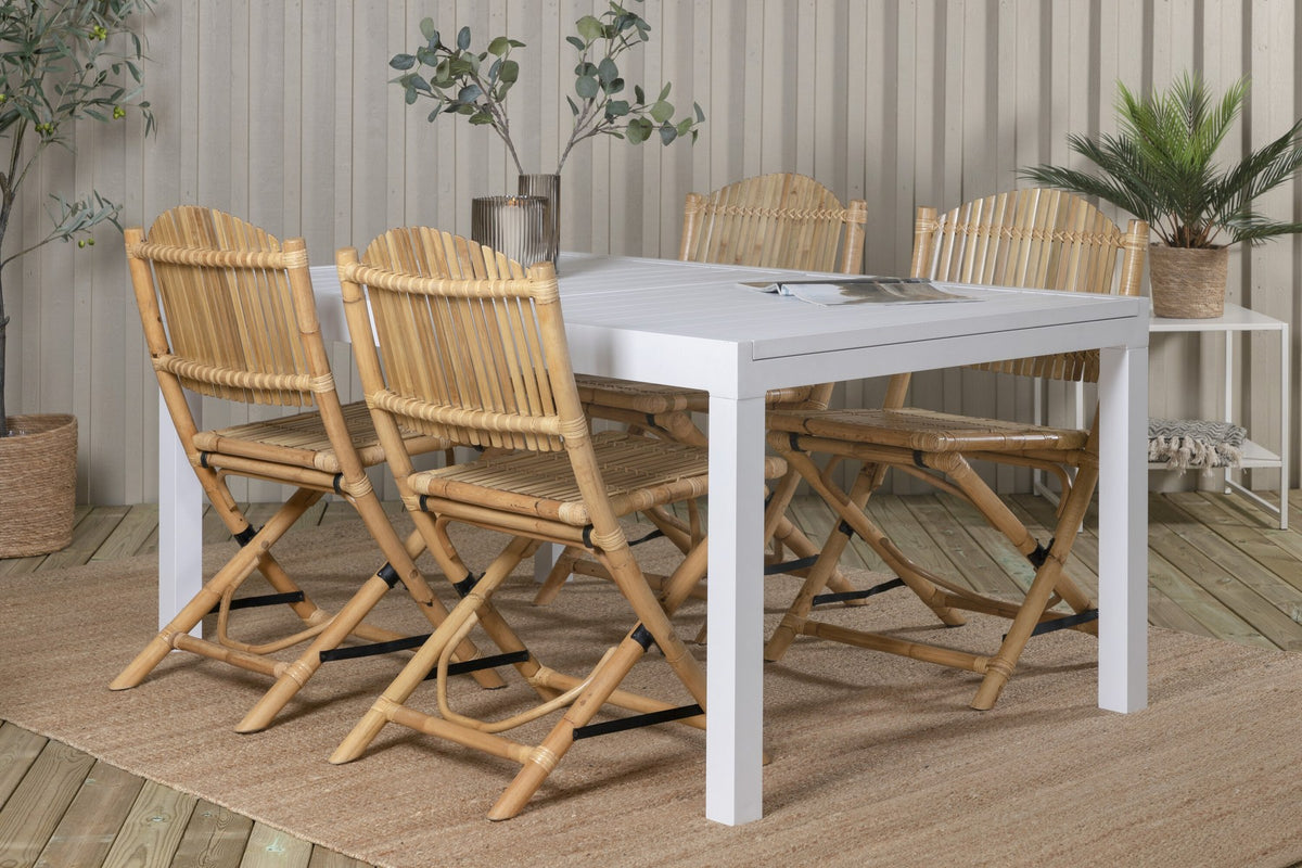 Aluminium-Caféstuhl in Natur mit Baumwoll-Polyester-Bezug neben rechteckigem Esstisch mit weisser Aluminium-Tischplatte und Rattanbeinen.