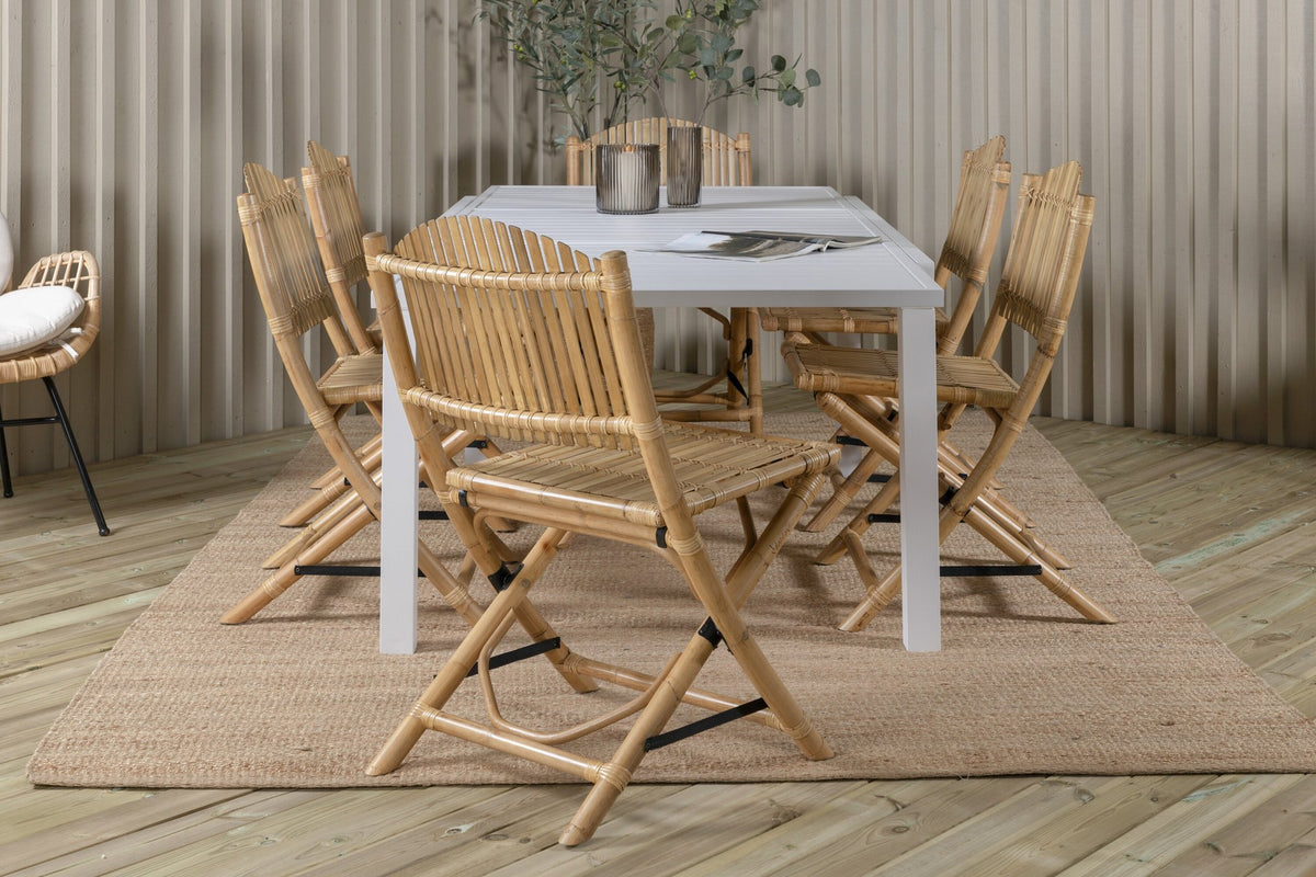 Aluminium-Caféstuhl in Natur mit Baumwoll-Polyester-Bezug neben rechteckigem Esstisch mit weisser Aluminium-Tischplatte und Rattanbeinen.