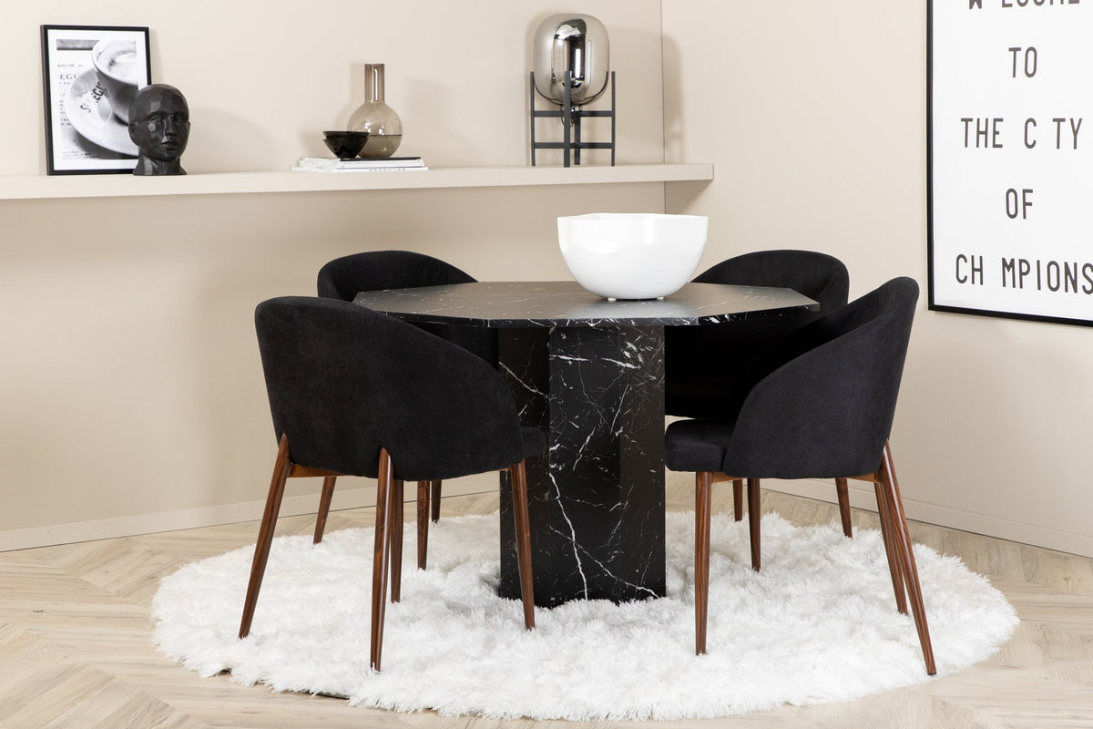 Zwei schwarze Esszimmerstühle mit Nussbaum-Beinen und Polyester-Sitzfläche neben rundem Esstisch Ø110cm mit schwarzer MDF-Platte und Stahlbeinen.