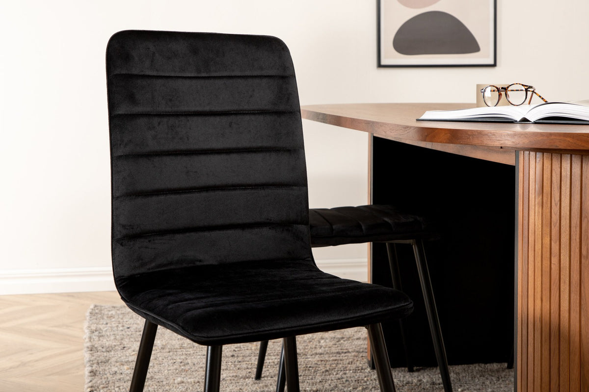 Ovaler Esstisch mit Nussbaum-Tischplatte aus MDF und Furnier sowie zwei schwarze Esszimmerstühle mit Samtsitz und schmalen Beinen.