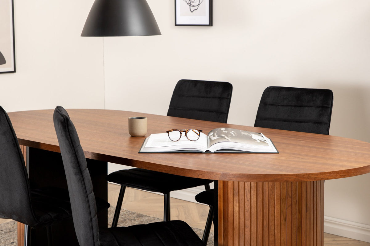 Ovaler Esstisch mit Nussbaum-Tischplatte aus MDF und Furnier sowie zwei schwarze Esszimmerstühle mit Samtsitz und schmalen Beinen.