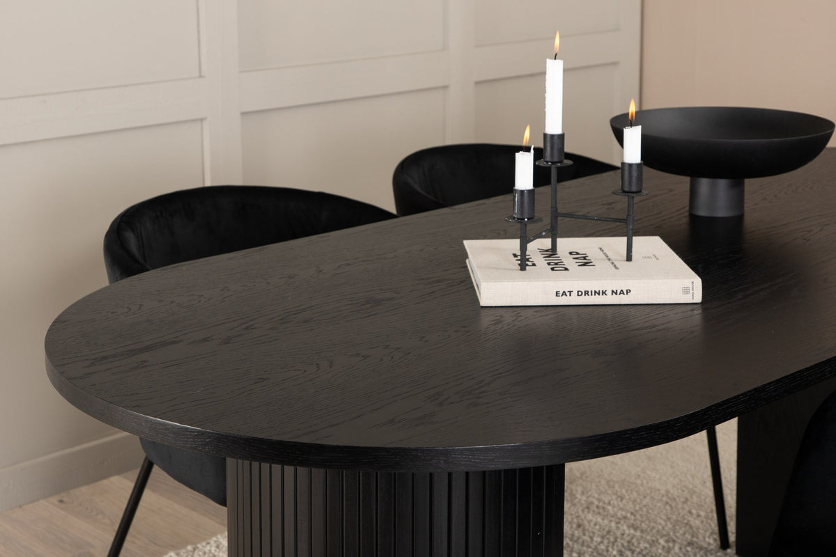 Schwarzes Esszimmerset aus MDF mit ovalem Esstisch und vier Stühlen mit Samtsitz und schlankem Eisengestell, Ansicht von vorne.