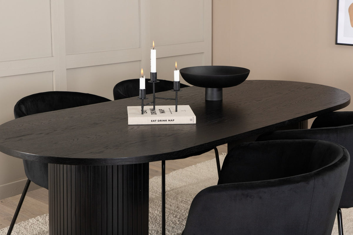 Schwarzes Esszimmerset aus MDF mit ovalem Esstisch und vier Stühlen mit Samtsitz und schlankem Eisengestell, Ansicht von vorne.