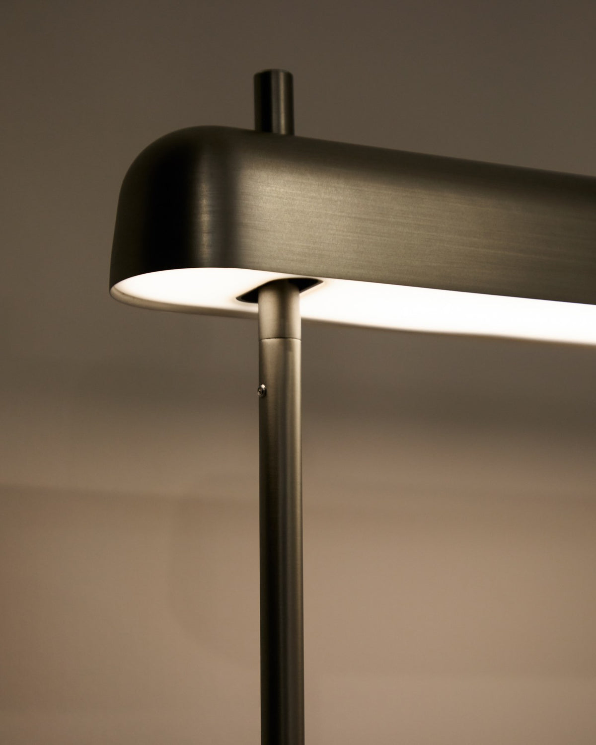 Graue Tischlampe Nelaia aus Stahl mit Kippschalter, Sockel aus Metall, schlanke zylindrische Form, LED-Leuchtmittel sichtbar.