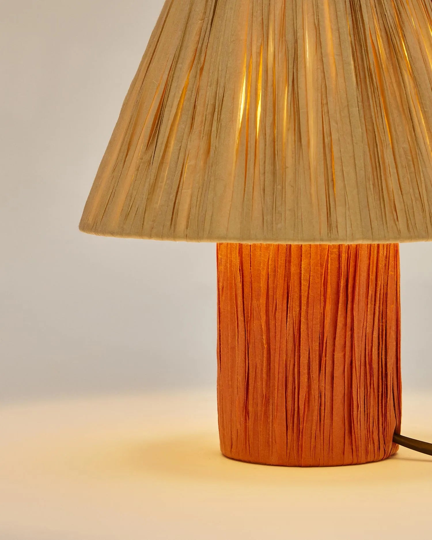 Die Pulmi Tischleuchte vereint Raffiabast in Natur und Terrakotta mit Massivholz für ein warmes, handgefertigtes Design.