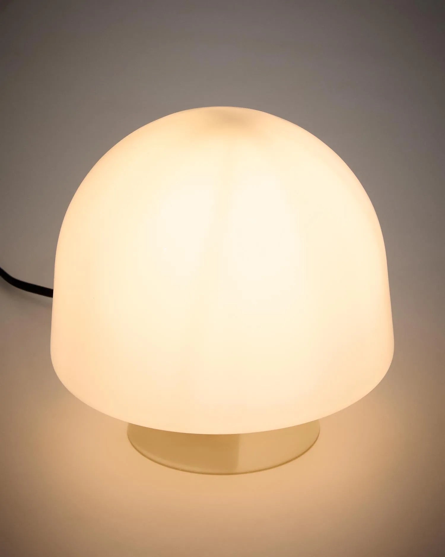 Die Tischleuchte Reig aus grauem Glas vereint Retro-Charme mit modernem Design und schafft ein warmes, diffuses Licht.