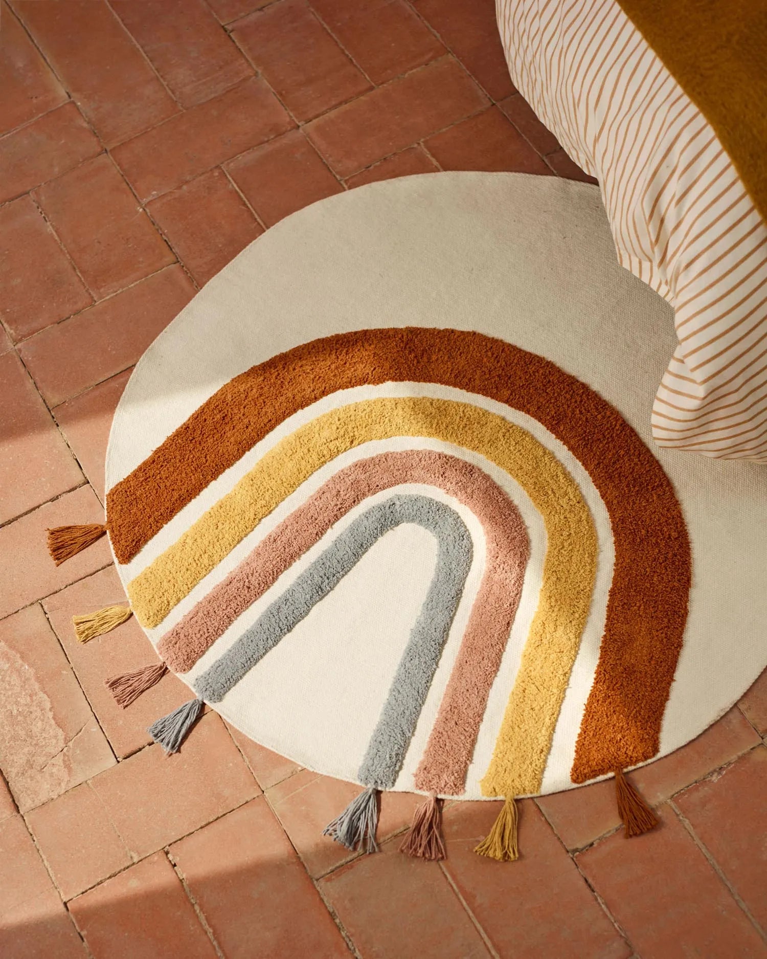 Ein bunter, runder Baumwollteppich (100 cm) mit Regenbogenmuster, ideal für fröhliche Kinderzimmer.